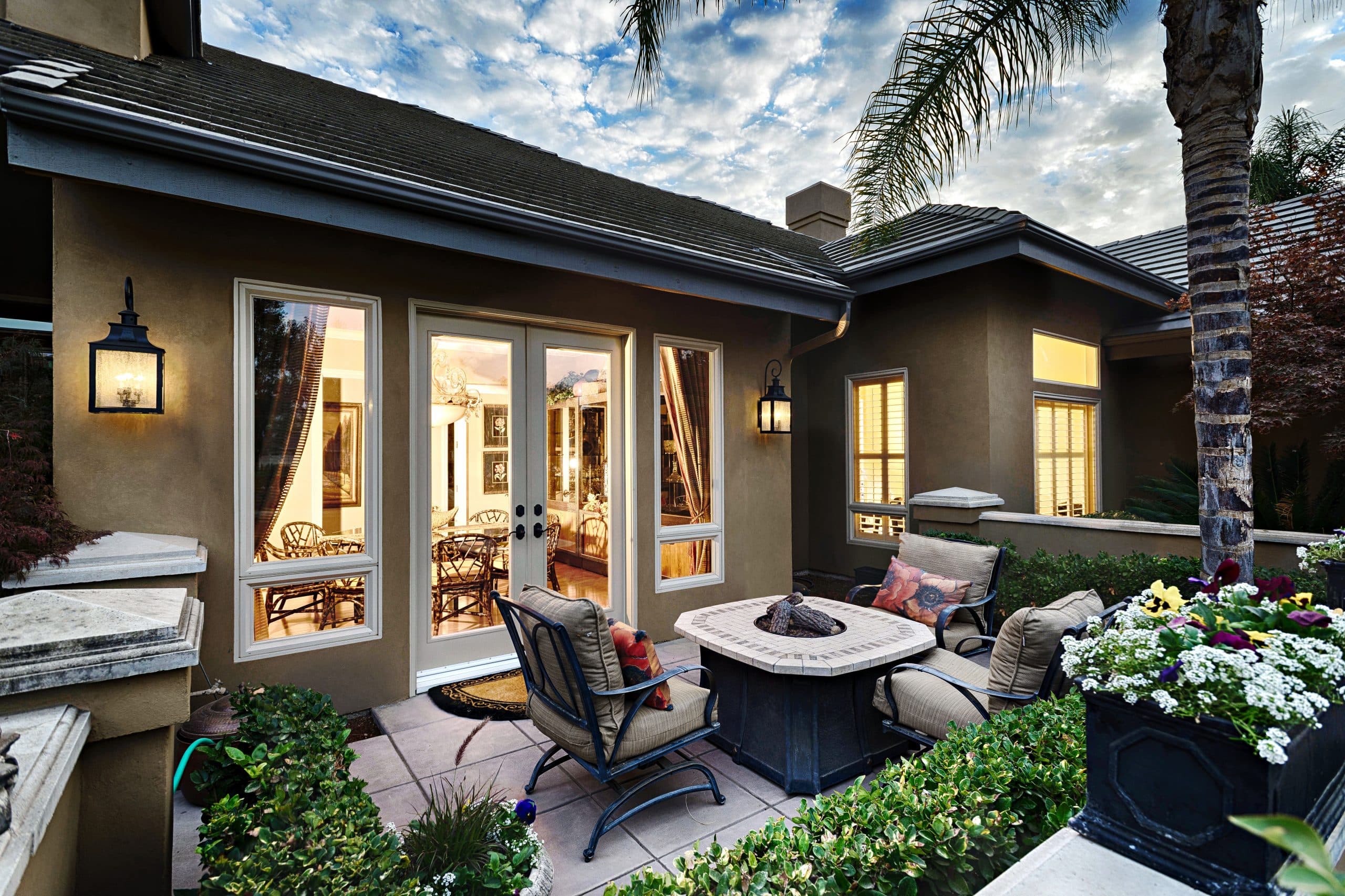 Twilight exterior shot of a stucco home with red tile roof — warm light glowing through white-frame Anlin windows and French doors over a back patio