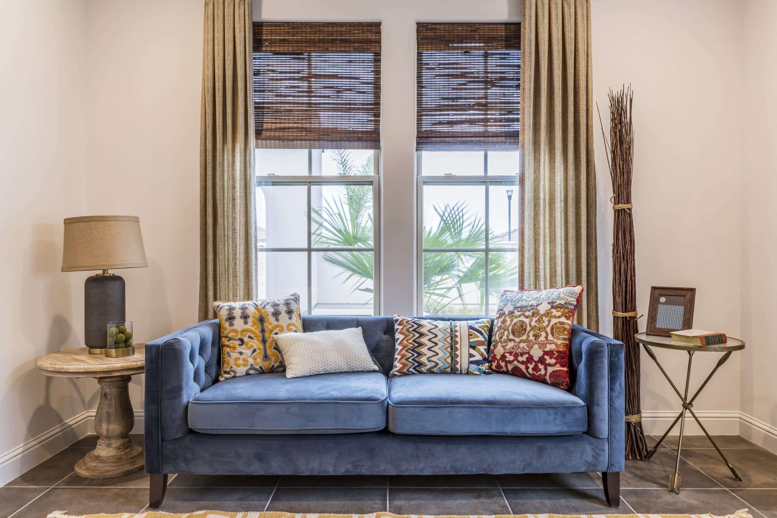 Living room with a pair of tall white-frame Anlin windows and woven roman shades above a blue velvet sofa